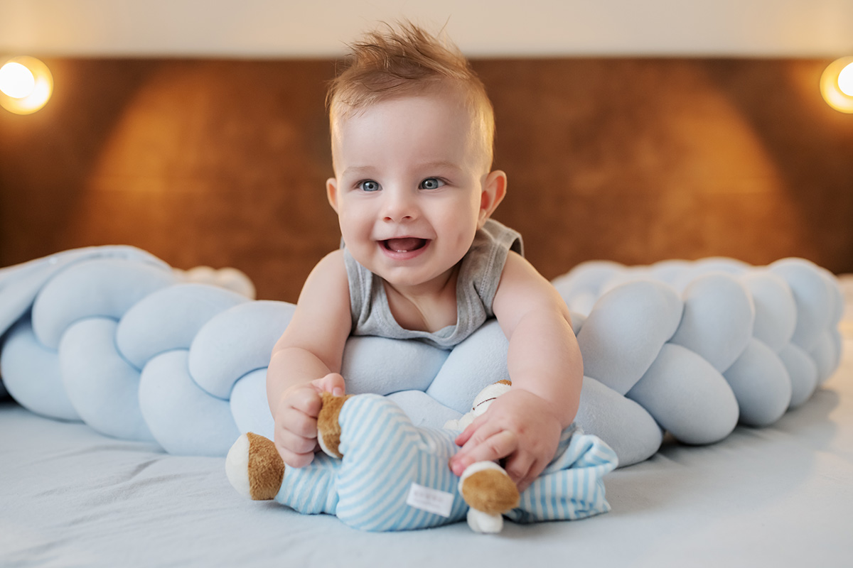 smiling baby playing with blue elephant toy on bed