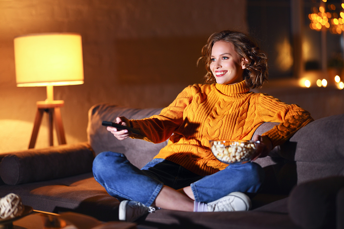 woman watching tv on her couch with a bowl of popcorn