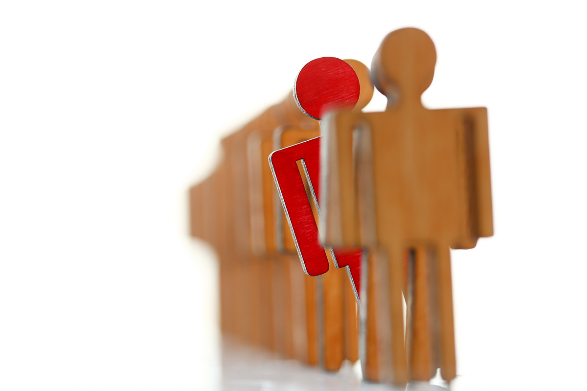 red wooden figure peeking out from line of non-painted wooden figures