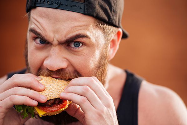 man aggressively eating a cheeseburger